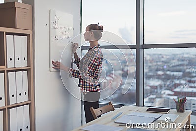 Businesswoman writing day plan on white magnet board, modern office. Side view of caucasian female employee planning Stock Photo