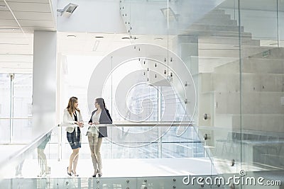 Businesswomen conversing against railing in office Stock Photo