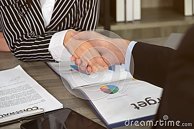 Businesswomen seated at office desk shaking hands with businessman after signed contract Stock Photo