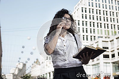 Businnes woman in office style clothing talking on the mobile phone with client and holding in hand her notebook Stock Photo