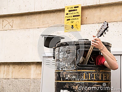 Busker singing and playing guitar inside a rubbish bin Stock Photo