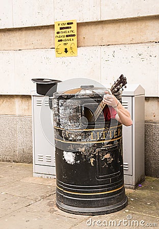 Busker singing and playing guitar inside a rubbish bin Stock Photo