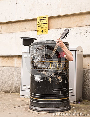 Busker singing and playing guitar inside a rubbish bin Stock Photo