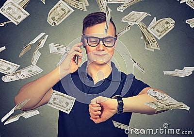 Busy businessman looking at wrist watch, talking on mobile phone under cash rain. Time is money concept Stock Photo