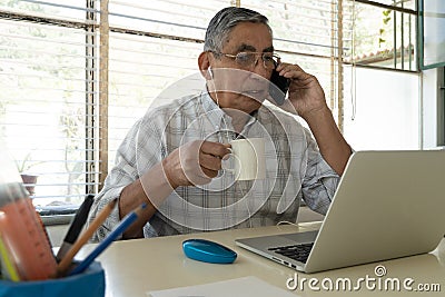 An elderly man drinks a cup of coffee sits at a laptop Stock Photo