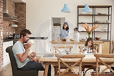 Busy Family Home With Father Working As Mother Prepares Meal Stock Photo