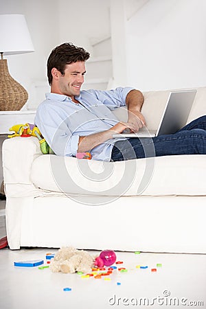 Busy father working on laptop on couch Stock Photo