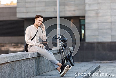 Busy guy solves business problems. Man speaks at smartphone and works on laptop Stock Photo
