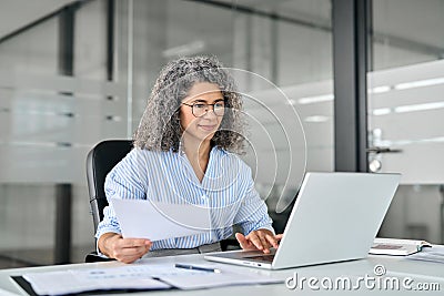 Busy mature business woman working in office with laptop and documents. Stock Photo