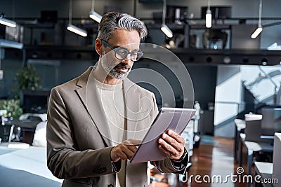 Busy mature older business man executive standing in office using tablet. Stock Photo