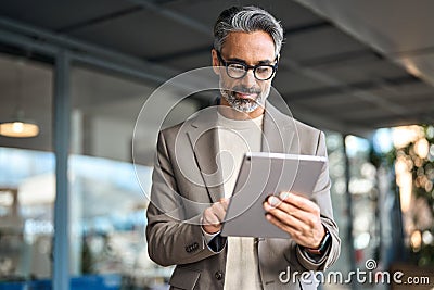 Busy mature older business man executive standing in office using tablet. Stock Photo