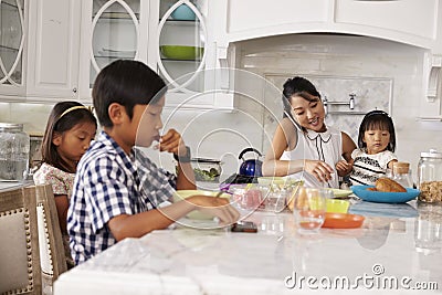 Busy Mother Organizing Children At Breakfast In Kitchen Stock Photo