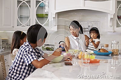 Busy Mother Organizing Children At Breakfast In Kitchen Stock Photo