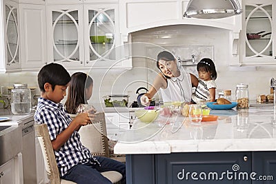 Busy Mother Organizing Children At Breakfast In Kitchen Stock Photo