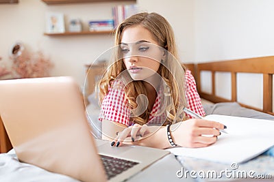 Busy teen student writing an assigment and participating at online class from home due to covid-19 global pandemic Stock Photo