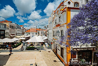 Busy touristic restaurants and bars with traditional Portuguese architecture and blue Jacaranda tree on foreground Editorial Stock Photo