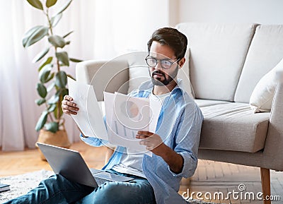 Busy Young Arab Entrepreneur Checking Papers And Using Laptop Computer At Home Stock Photo