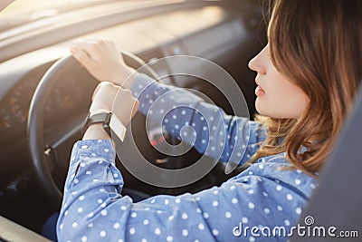 Busy young woman drives car and looks at watch, stuck in traffic jam, hurries to work, being nervous and stressed, feels impatient Stock Photo