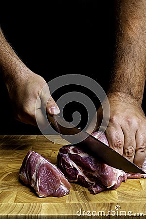 Butcher hands close up: cutting meet on wooden board on black Stock Photo