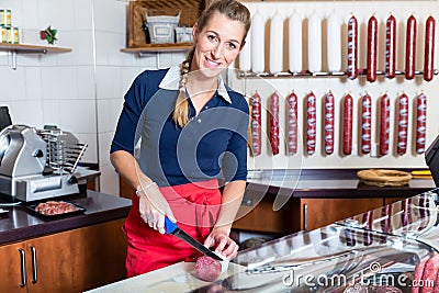 Butcher woman cutting a sausage in the shop Stock Photo