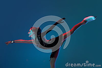 Dynamic portrait of young girl, female figure skater in black stage dress skating isolated on blue background in neon Stock Photo