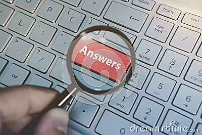 Button Answers on laptop keyboard viewed through the magnifier hold by male hand. Key answers on modern keyboard Stock Photo