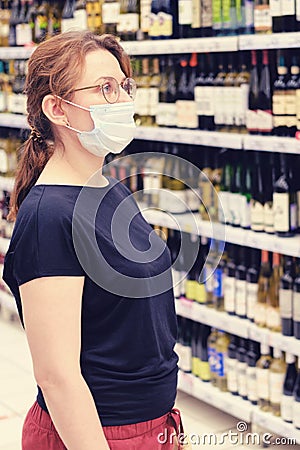 A buyer in a medical mask chooses wine in a supermarket. Sale of alcohol and drink in a store. Flu virus quarantine in public Stock Photo