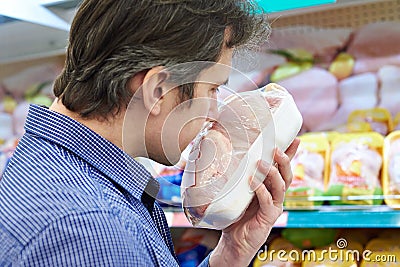 Buyer sniffing chicken in store, checking freshness Stock Photo