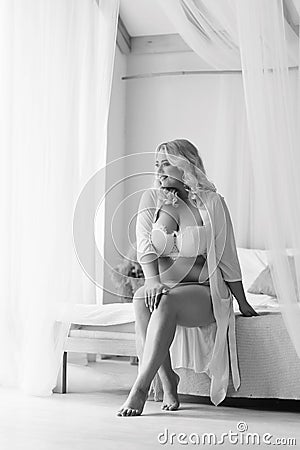 Bw blonde girl plus size sitting on the bed in white lingerie portrait of Bali morning bride Stock Photo