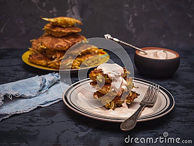 Cabbage oladi are lying on a plate, watered with sour cream, denim napkin, cutlery. In the background is a large plate with Stock Photo