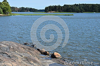Cabin and forests across a rocky lake`s shore. Stock Photo