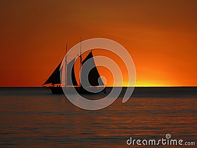 A sail boat silhouetted against a golden sunset Stock Photo