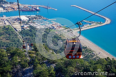 Cable car to the mountain next to the clean blue ocean with industrial port in the background - Antalya (Turkey) Stock Photo