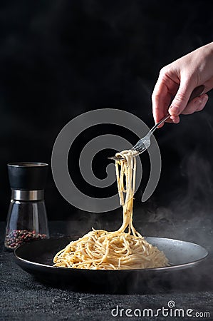 Cacio e Pepe - Hot Italian Pasta with Cheese and Pepper on Black Plate, Woman Holding Fork Spaghetti on Dark Background Stock Photo