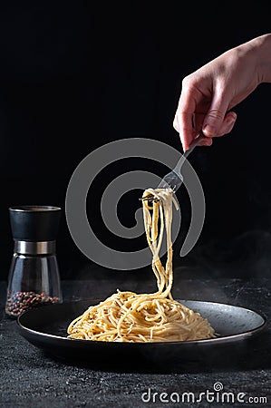 Cacio e Pepe - Hot Italian Pasta with Cheese and Pepper on Black Plate, Woman Holding Fork Spaghetti on Dark Background Stock Photo