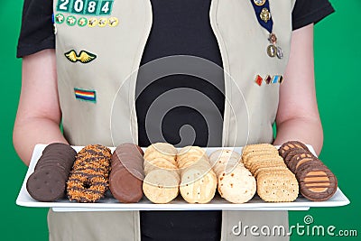 Cadette Girl Scout holding plate of Girl Scout cookies on green background Editorial Stock Photo