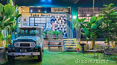 The outdoor terrace of a cafe with green synthetic grass, plants, and a jeep as decorations Editorial Stock Photo