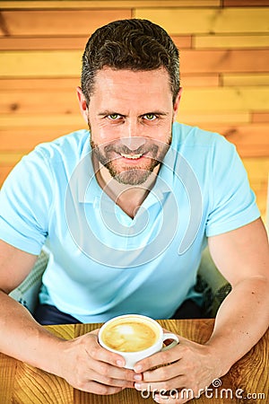 Cafe visitor happy face enjoy coffee caffeine drink. Man bearded guy drinks cappuccino at wooden table cafe. Caffeine Stock Photo