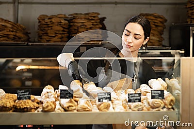 Cafe waitress girl puts fresh pastries on the cafe showcase, bakery worker Stock Photo