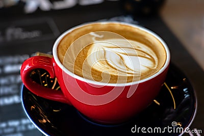 Caffee latte macchiato cappuccino in red mug in cafe house with milk foam art Stock Photo