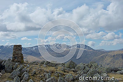 Cairn and rocks at summit of Lake District mountain; snow covered crags in distance Stock Photo