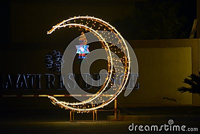 Cairo, Egypt, April 17 2023: A crescent made with led lights with Ramadan Fanous lamp lantern in the street as a festive sign Editorial Stock Photo