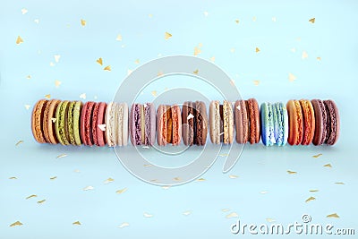 Cake french macaroons, sweet colorful macarons stand in row and gold confetti on light blue background. Birthday holiday party Stock Photo