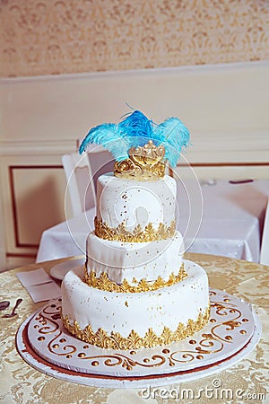 The cake has blue feathers and a golden crown . White three-tiered cake Editorial Stock Photo