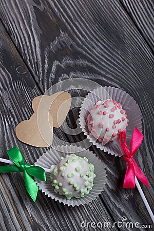 Cake pops in white glazed chocolate with green and pink sprinkles. A green and pink bow is tied on sticks. Nearby hearts cut out Stock Photo