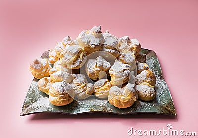 Cakes profiteroles sprinkled with powdered sugar on a pink background. Homemade eclairs. Stock Photo