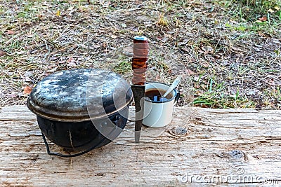 A caldron, a knife and a mug on a wooden stand in outdoor. Tourist. Stock Photo