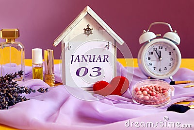 Calendar for January 3: decorative house with the name of the month in English, number 03, various cosmetics, white alarm clock, Stock Photo