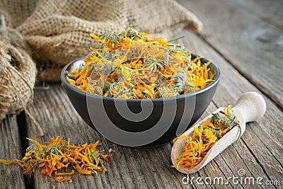 Calendula flowers in bowl, wooden scoop of dry marigold petals and canvas sack on background. Herbal medicine Stock Photo