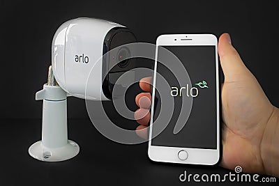 An Arlo security camera with an iPhone Plus hold by a person using the Arlo aplication Editorial Stock Photo